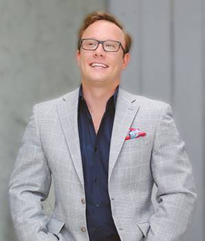 a man in a suit and glasses standing with his hands in his pockets.