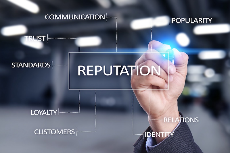 A hand writes the word "REPUTATION" on a transparent screen, surrounded by related terms inspired by reputation theory: communication, popularity, trust, standards, loyalty, customers, relations, and identity. The background is blurred.