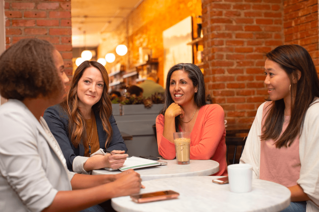 a group of women sitting around a table talking.