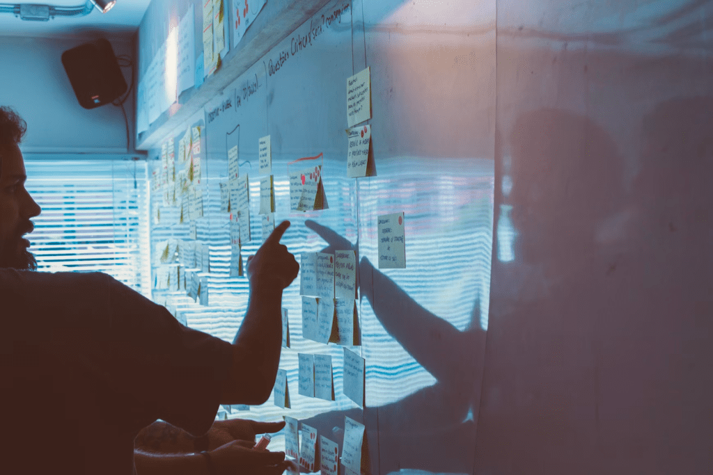 a man and a woman are pointing at sticky notes on a wall.