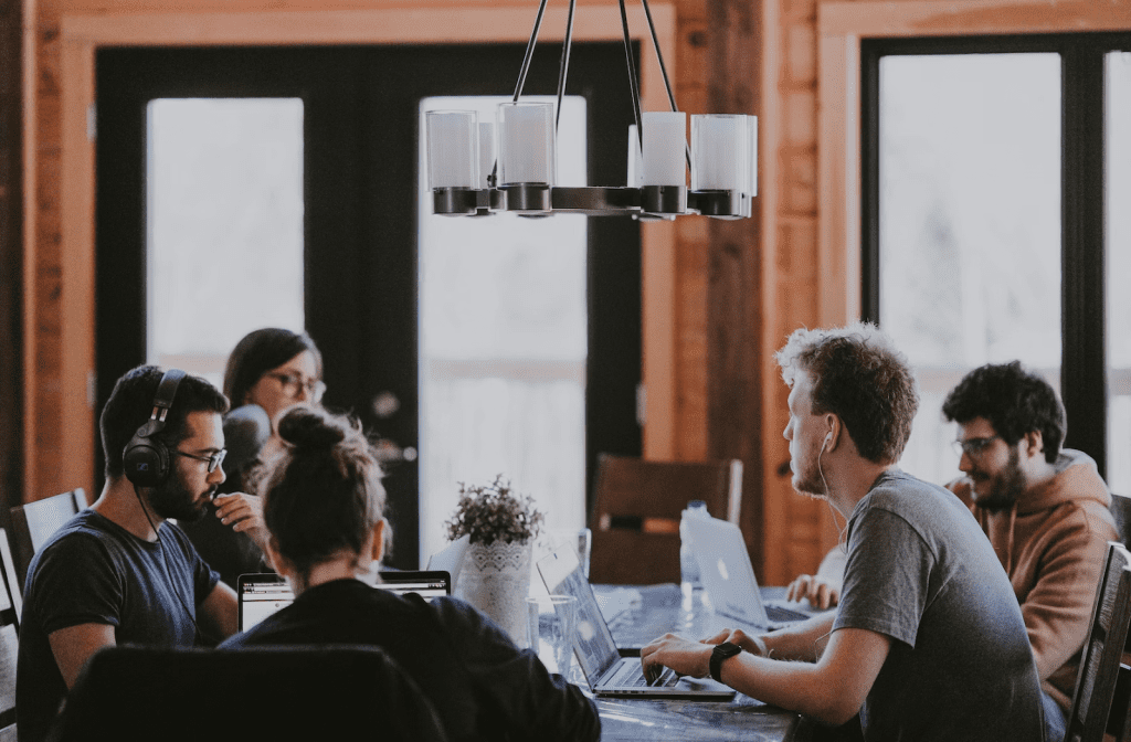 a group of people sitting around a table with laptops.