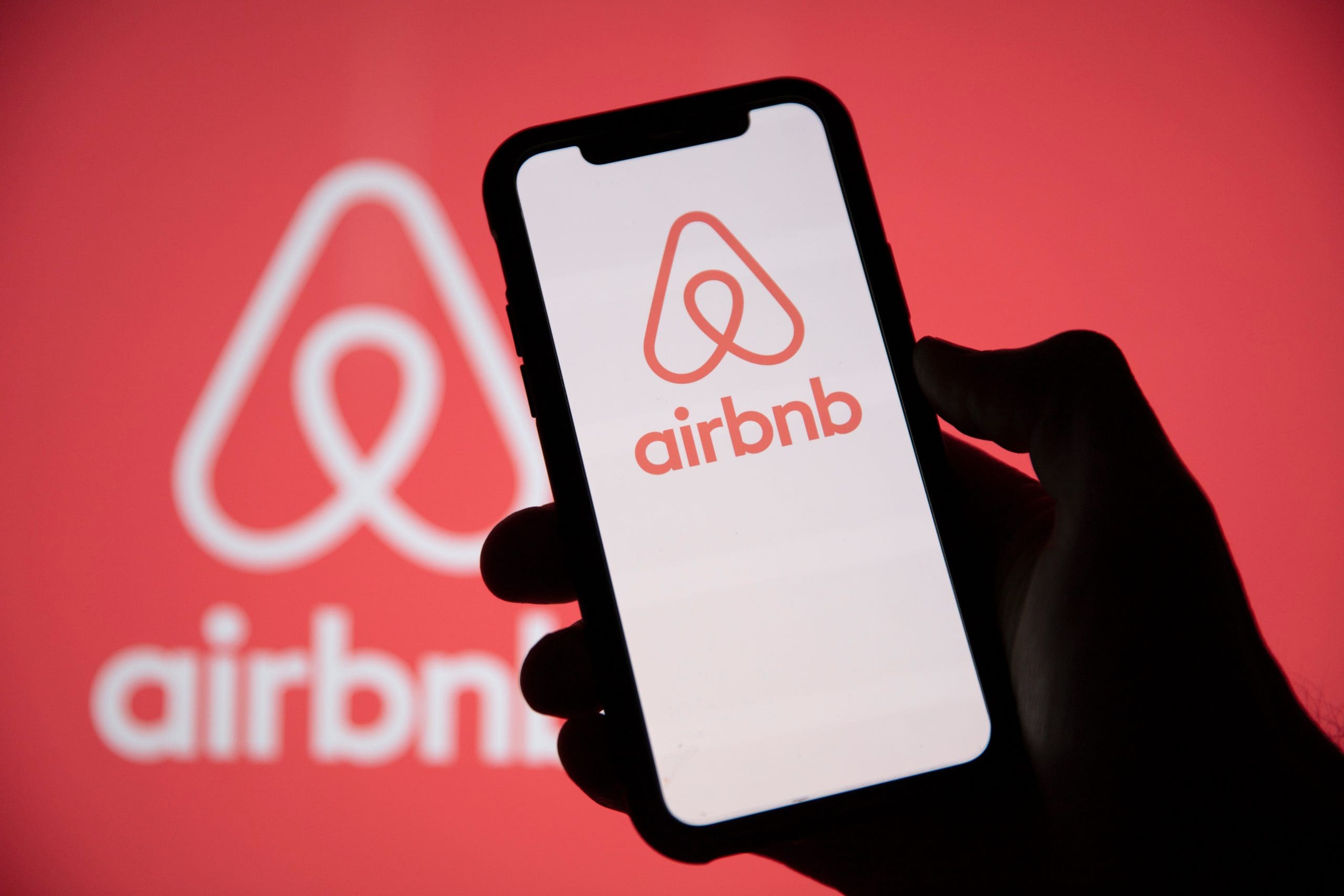 The airbnb logo is displayed on a person's phone.