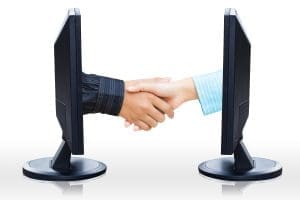 Two people shaking hands in front of two monitors.