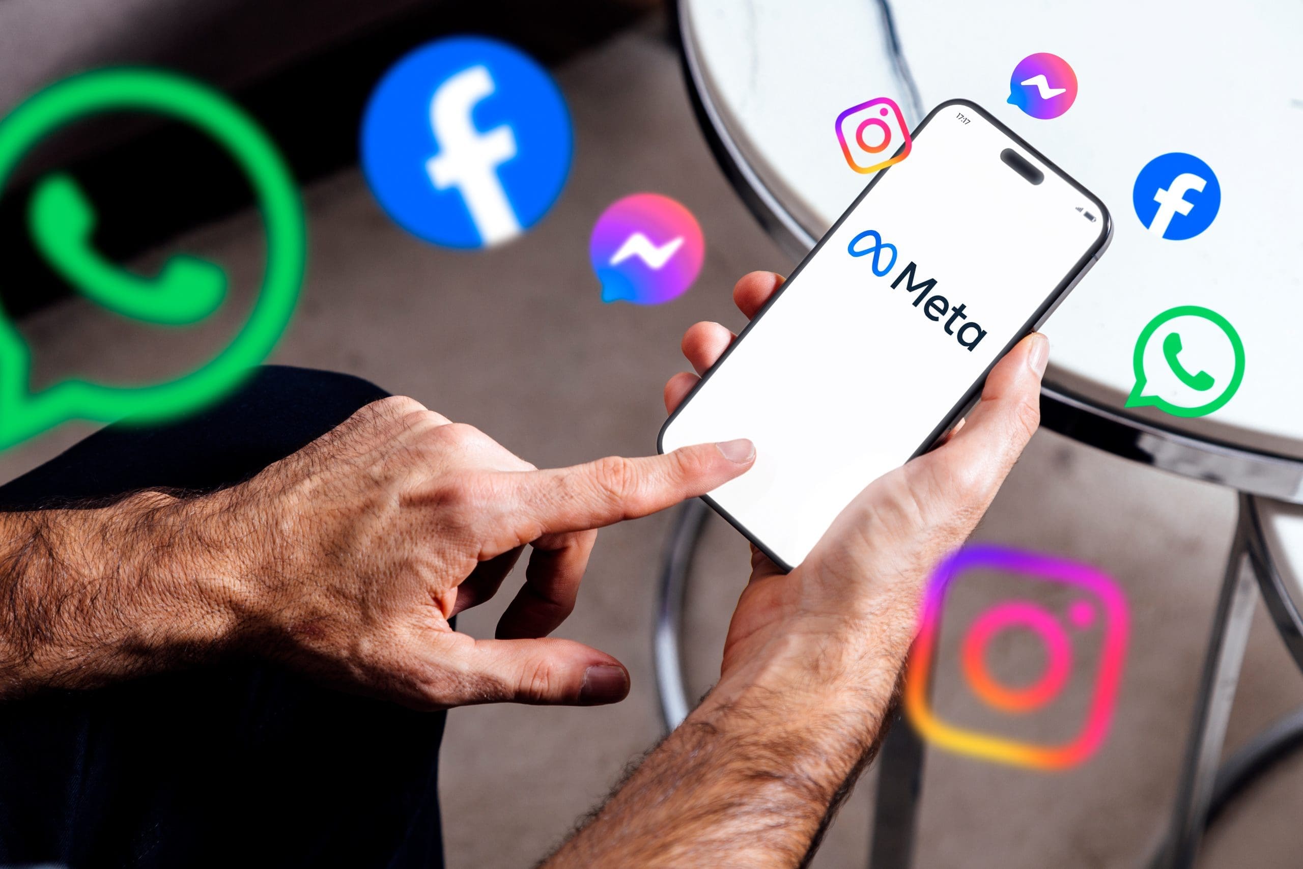 A person holds a smartphone displaying the Meta logo, surrounded by digital icons of Facebook, Instagram, WhatsApp, and Messenger, suggesting Meta's ownership of these social media platforms.