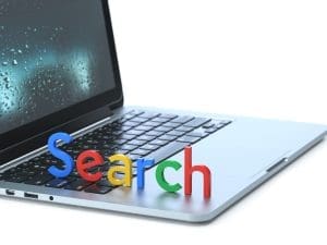 A laptop with colorful 3D letters spelling “Search” placed on its keyboard. The screen shows raindrops on a window, and the background is white.