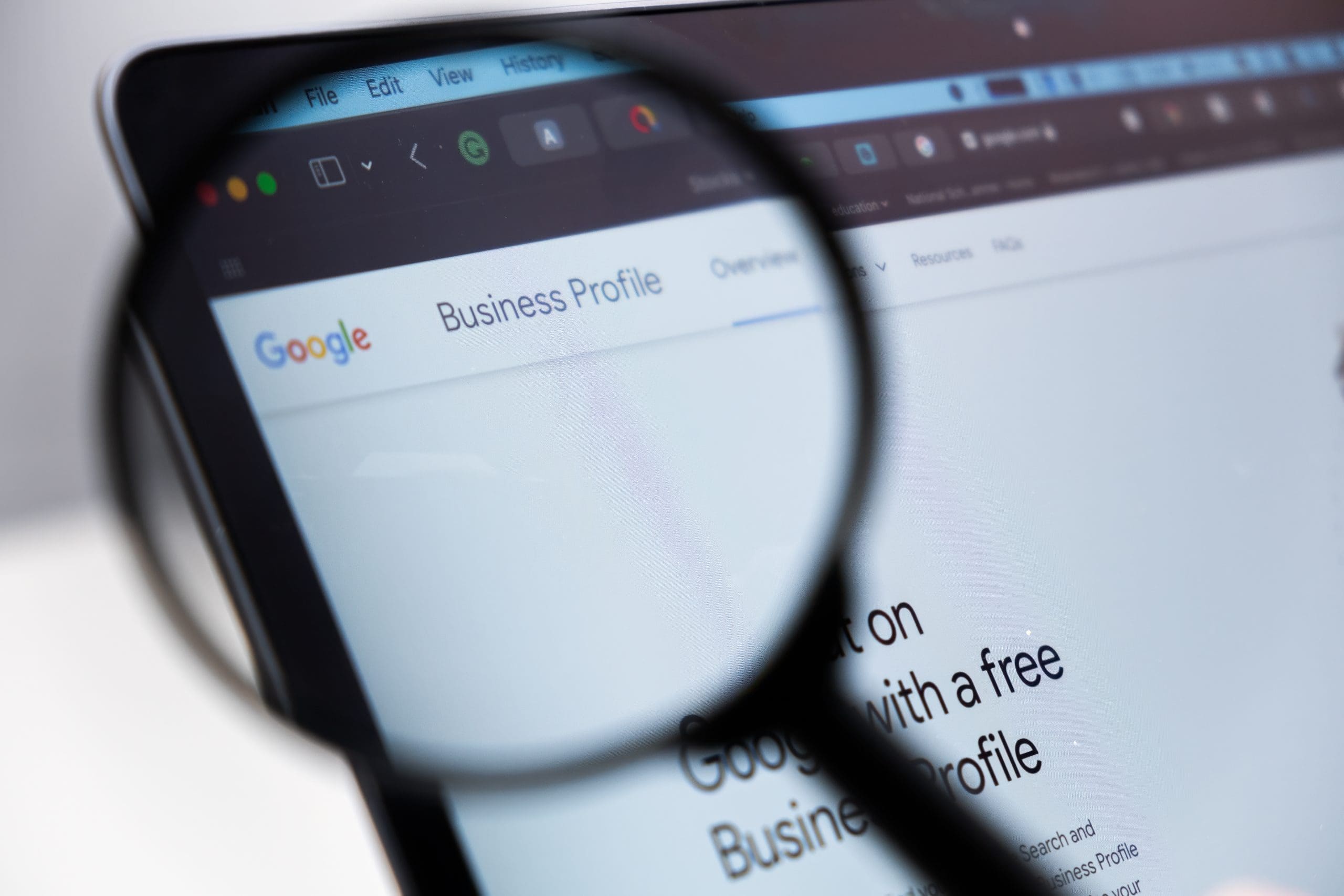 A magnifying glass focuses on a computer screen displaying the Google Business Profile webpage, highlighting the "Business Profile" tab in a web browser.