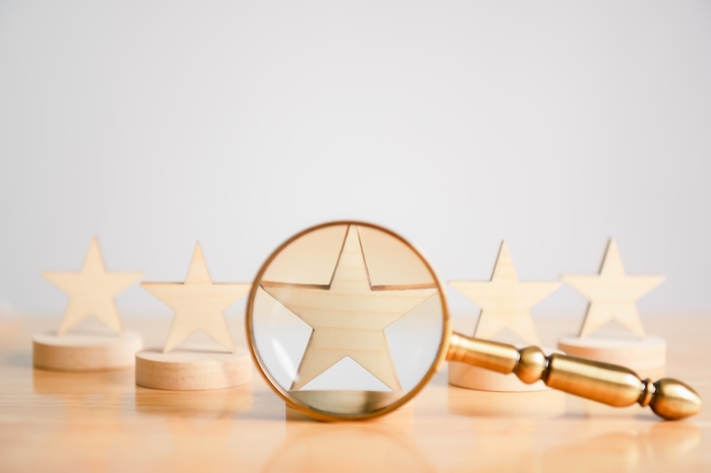A row of wooden stars on round bases sits on a table. A magnifying glass in the foreground focuses on the center star—much like how does Google detect fake reviews, it highlights key details and uncovers authenticity.