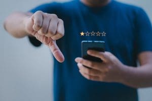 A person holds a phone and gives the thumbs-down sign, indicating the worst customer service companies have received low-star reviews.
